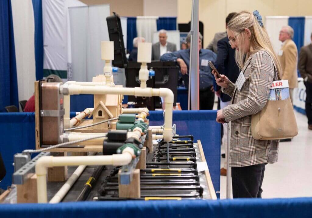 female exhibit attendee photographing pipefitting equipment